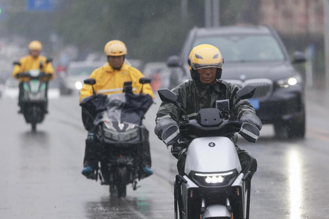 今年5月17日的北京街头,外卖骑手在雨中进行配送。(中新社)